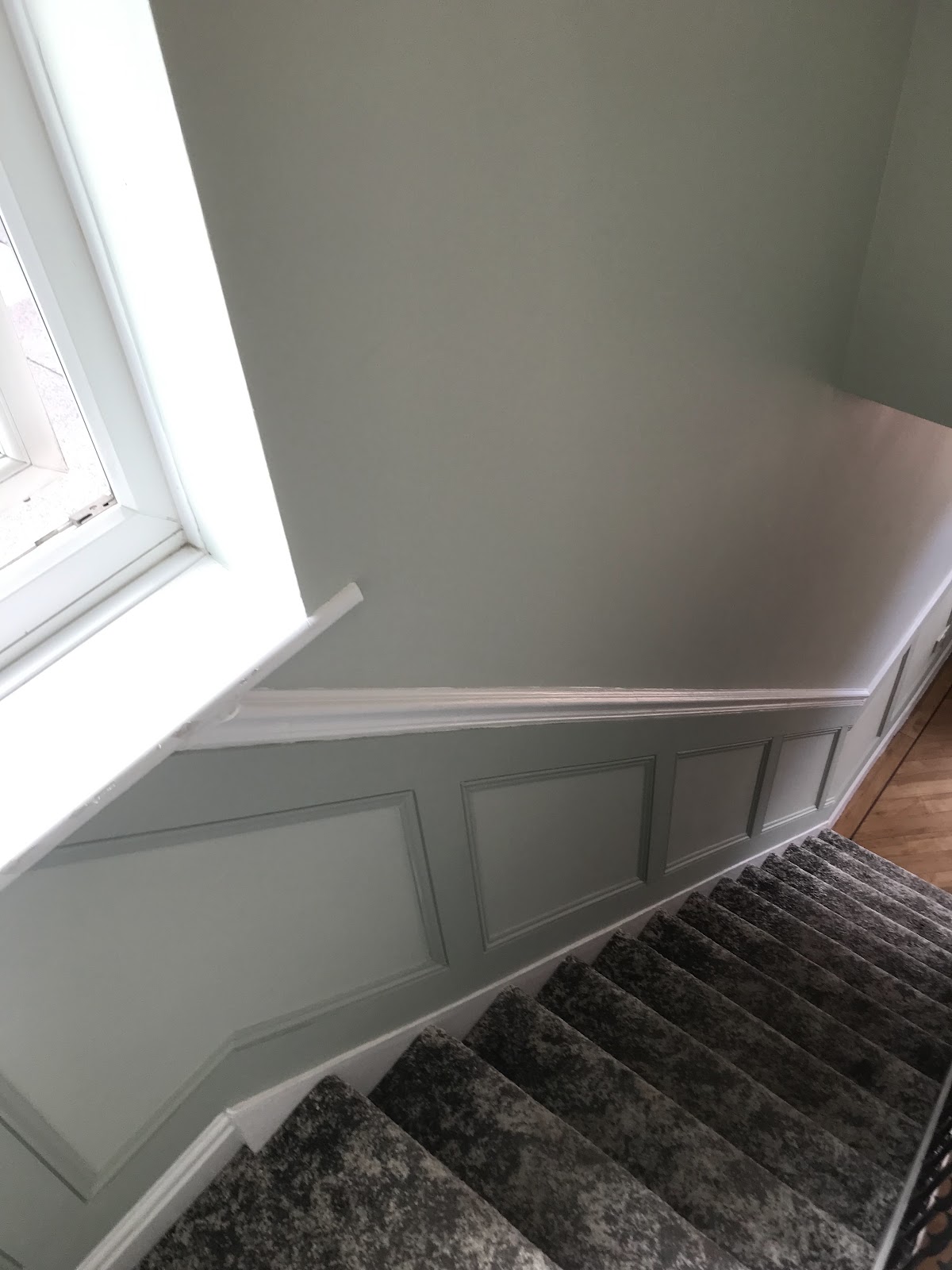 Stairwell decorated in sage green with white panelled wainscoting